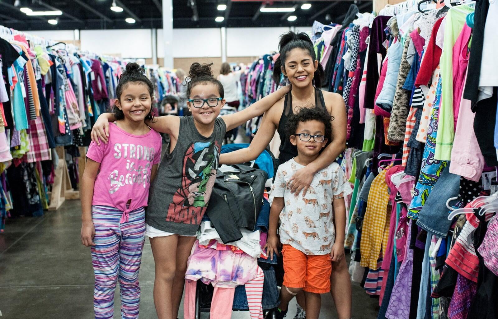 A mom and her three kids stand in front of a rack of girls clothes at their local BF sale.